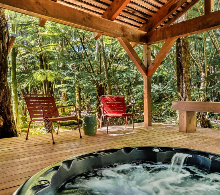 romantic hot tub on a cedar lanai in rainforest with two red patio chairs and wooden bench