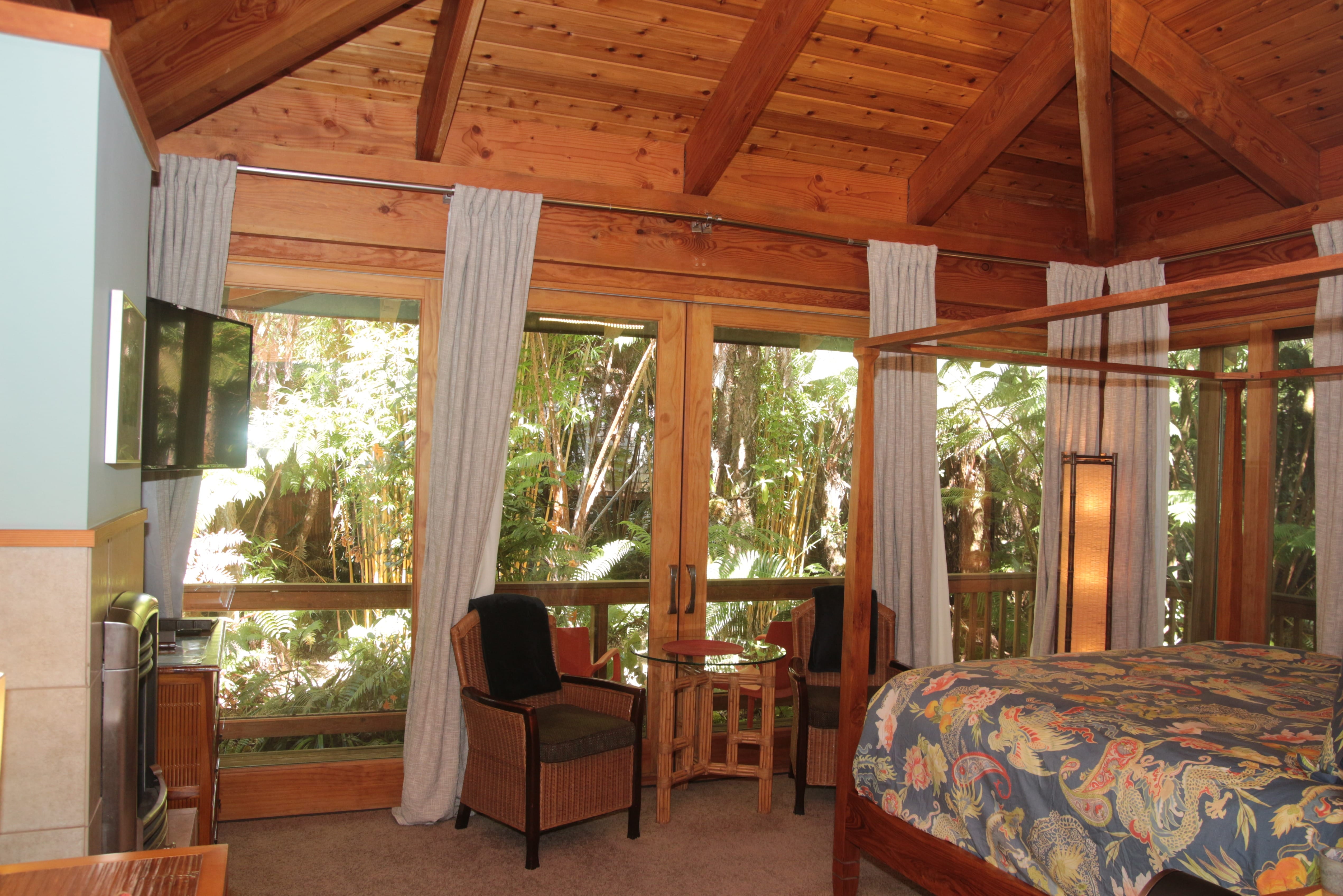 view of Haiku Garden suite including bed, two sitting chairs, high ceilings, and rainforest view